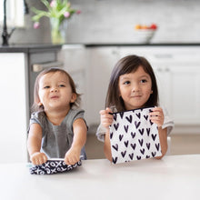 Load image into Gallery viewer, Two kids sit at a white table in a kitchen, each holding a Bumkins Reusable Snack Bag, Large 2-Pack: XOXO & Hearts.