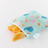 Orange slices peek out from a Bumkins Reusable Snack Bag, Large 2-Pack: Ocean Life & Whale Tail on a white background.