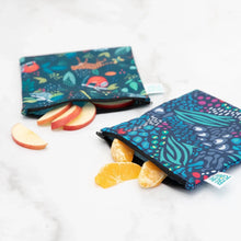 Load image into Gallery viewer, Bumkins Reusable Snack Bag, Large 2-Pack: Jungle & Animal Prints holds apple and orange slices on a marble surface.