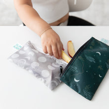 Load image into Gallery viewer, A child's hand reaches for apple slices from Bumkins Reusable Snack Bag, Small 2 Pack: Desert Night on a white table.