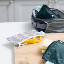 Load image into Gallery viewer, A Bumkins Reusable Snack Bag, Small 2 Pack: Desert Night rests on a cutting board with yellow bell pepper slices peeking out.