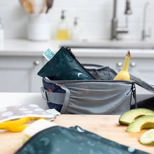 Load image into Gallery viewer, A Bumkins Reusable Snack Bag, Small 2 Pack: Desert Night sits in a lunchbox with a banana on a kitchen counter surrounded by food and bags.