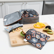 Load image into Gallery viewer, A Bumkins Reusable Snack Bag, Small 2 Pack: Everyday Is Halloween sits on a cutting board on a kitchen counter with food next to a lunch bag.