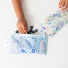 Load image into Gallery viewer, A child's hand reaches for blueberries next to Bumkins Reusable Snack Bag, Small 2 Pack: Stitch Star-ring Up Trouble on a white table.