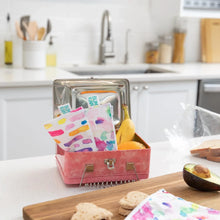 Load image into Gallery viewer, Bumkins Reusable Snack Bag, Small 2-Pack: Watercolor & Brush Strokes sits in a metal lunch box with a banana and orange on a kitchen counter.