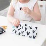 Close-up of a child in white dress holding a berry above Bumkins Reusable Snack Bag, Small 2-Pack: XOXO & Hearts on a white table.