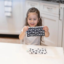 Load image into Gallery viewer, A young girl holds a Bumkins Reusable Snack Bag, Small 2-Pack: XOXO & Hearts, while the other lies on a white table.