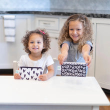 Load image into Gallery viewer, Two girls smile at a white table with Bumkins Reusable Snack Bag, Small 2-Pack: XOXO & Hearts.