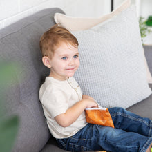 Load image into Gallery viewer, A toddler on a gray sofa smiles, holding a Bumkins Reusable Snack Bag 4 Pack: Desert Boho.