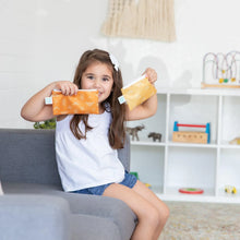 Load image into Gallery viewer, A girl smiles on a gray couch, holding two bags from Bumkins Reusable Snack Bag 4 Pack: Desert Boho.