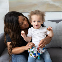 Load image into Gallery viewer, A curly-haired toddler sits on a woman's lap on a gray couch as she opens a Bumkins Reusable Snack Bag, Small 2-Pack: Super Mario™.