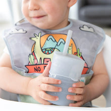 Load image into Gallery viewer, A toddler with a colorful dinosaur bib holds a Bumkins Silicone Straw Cup with Lid: Gray.