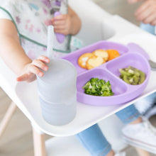 Load image into Gallery viewer, A child in a high chair reaches for a Bumkins Silicone Straw Cup with Lid: Gray next to a lavender plate.