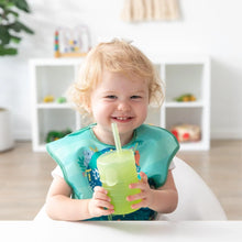 Load image into Gallery viewer, A toddler joyfully holds a Bumkins Silicone Straw Cup with Lid: Sage at a white table.