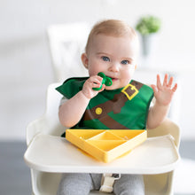 Load image into Gallery viewer, A baby in a high chair wears a Bumkins Caped SuperBib®: The Legend of Zelda™ Link, chewing a green spoon near a yellow triangle plate.