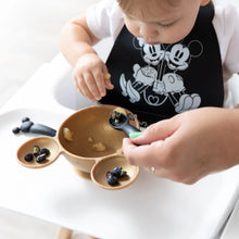Load image into Gallery viewer, A toddler in a high chair eats from a bowl, assisted by an adult hand with a Bumkins Silicone Dipping Spoons: Mickey Mouse (Classic Black).