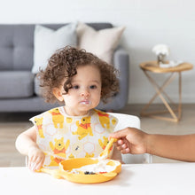 Load image into Gallery viewer, A curly-haired toddler eats with adult help from a dish with Bumkins Silicone Dipping Spoons: Winnie the Pooh, food smudged on their cheeks.
