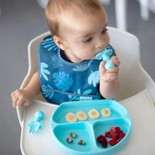 Load image into Gallery viewer, A baby in a high chair wearing a blue bib uses Bumkins Silicone Chewtensils®: Blue to eat fruit from a blue divided plate.