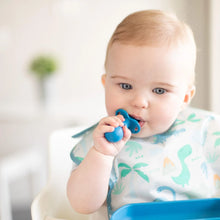 Load image into Gallery viewer, A baby in a high chair, wearing a dinosaur bib, looks intently at a blue plate while chewing a Bumkins Silicone Chewtensils®: Dark Blue.
