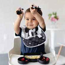 Load image into Gallery viewer, A toddler in a high chair holds Bumkins Silicone Chewtensils®: Mickey Mouse above their head while a black plate of food sits on the tray.