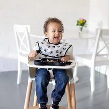 Load image into Gallery viewer, A happy toddler in a high chair, wearing a black & white bib, eats from a black plate with Bumkins Silicone Chewtensils®: Mickey Mouse.