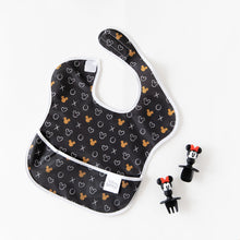 Load image into Gallery viewer, Bumkins Silicone Chewtensils®: Minnie Mouse rest next to a black & white Minnie Mouse-patterned bib on a white background.