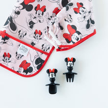 Load image into Gallery viewer, Bumkins Silicone Chewtensils®: Minnie Mouse rest next to a folded Minnie Mouse-patterned bib on a white background.