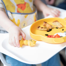Load image into Gallery viewer, Close-up of a child in a high chair reaching for Bumkins Silicone Chewtensils®: Winnie The Pooh next to a bear-shaped plate of food.