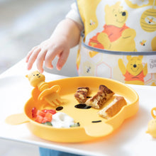 Load image into Gallery viewer, Close-up of a baby in a high chair reaching for Bumkins Silicone Chewtensils®: Winnie The Pooh on a bear-shaped plate with breakfast.