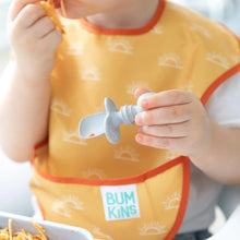 Load image into Gallery viewer, Close-up of a child wearing a yellow bib holding a Bumkins Silicone Chewtensils®: Gray.