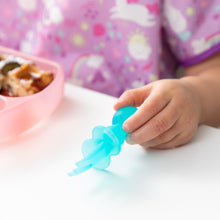 Load image into Gallery viewer, Close-up of a child holding Bumkins Silicone Chewtensils®: Blue Jelly near a pink sectioned plate, dressed in a unicorn-patterned bib.
