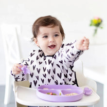 Load image into Gallery viewer, A happy toddler in a high chair wearing a heart-print bib holds eats from a purple plate with Bumkins Silicone Chewtensils®: Lavender.