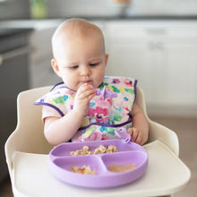 Load image into Gallery viewer, A baby in high chair wearing colorful bib holds Bumkins Silicone Chewtensils®: Lavender while eating from a divided plate.
