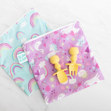 Load image into Gallery viewer, Two colorful unicorn and rainbow patterned bags lay on a marble background, with Bumkins Silicone Chewtensils®: Pineapple on top.