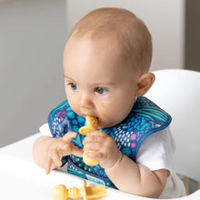 Load image into Gallery viewer, A baby in a high chair wearing a blue animal-print bib chews Bumkins Silicone Chewtensils®: Pineapple.
