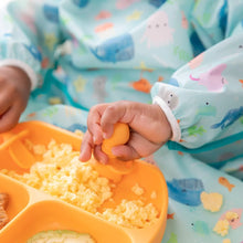 Load image into Gallery viewer, Close-up of a child in a blue sea-themed bib enjoying eggs from an orange divided plate using Bumkins Silicone Chewtensils®: Tangerine.