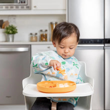 Load image into Gallery viewer, A toddler in a high chair wears a colorful bib, eating from an orange plate with Bumkins Silicone Chewtensils®: Tangerine.
