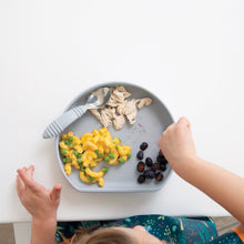 Load image into Gallery viewer, A child enjoys shredded chicken, mac and cheese with peas, and grapes from a gray plate using Bumkins Spoon + Fork: Gray at a white table.