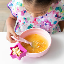 Load image into Gallery viewer, A child wearing a bright patterned bib enjoys soup from Bumkins Silicone Grip Bowl: Pink at a white table, using a spoon.