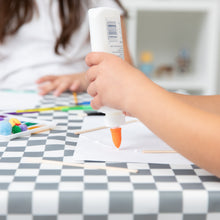 Load image into Gallery viewer, A child crafts with glue and other colorful art supplies on a Bumkins Splat Mat: Charcoal Check.