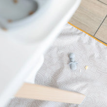 Load image into Gallery viewer, Aerial view of a Bumkins Splat Mat: Wander on a wood floor under a high chair, with a baby spoon and food on top.