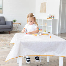 Load image into Gallery viewer, A young girl glues paper on a Bumkins Splat Mat: Wander, surrounded by craft supplies in a bright living room.