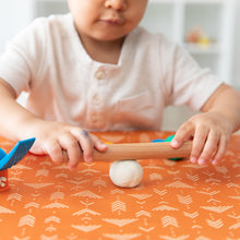 Load image into Gallery viewer, A child rolling dough on a table covered with a Bumkins Splat Mat: Grounded for mess-free fun.