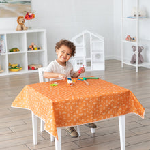 Load image into Gallery viewer, A child beams at a table with toys covered with a Bumkins Splat Mat: Grounded, in a playroom filled with shelves and stuffed animals.