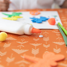 Load image into Gallery viewer, Close-up of a bottle of glue dripping on a Bumkins Splat Mat: Grounded, surrounded by colorful paper shapes, pom-poms, and craft materials.