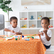 Load image into Gallery viewer, Two kids doing arts and crafts at a table covered with a Bumkins Splat Mat: Grounded, surrounded by art supplies in a bright room.