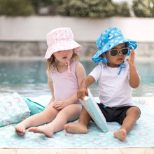 Load image into Gallery viewer, Two kids sit by a pool on Bumkins Splat Mat: Rainbows—one in a pink hat and swimsuit, the other in a blue hat, sunglasses, and white shirt.
