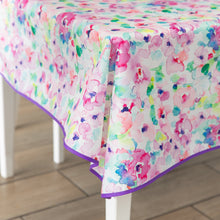 Load image into Gallery viewer, Bumkins Splat Mat: Watercolor in pink, purple, blue, and green hues with a purple trim drapes over a white table.