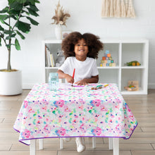 Load image into Gallery viewer, A child smiles while painting on a table covered with a Bumkins Splat Mat: Watercolor. A bookshelf and plant add charm to the background.