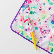 Load image into Gallery viewer, Close-up of Bumkins Splat Mat: Watercolor, colorful and stain-resistant, on a white background with a paint brush and paint smear on top.